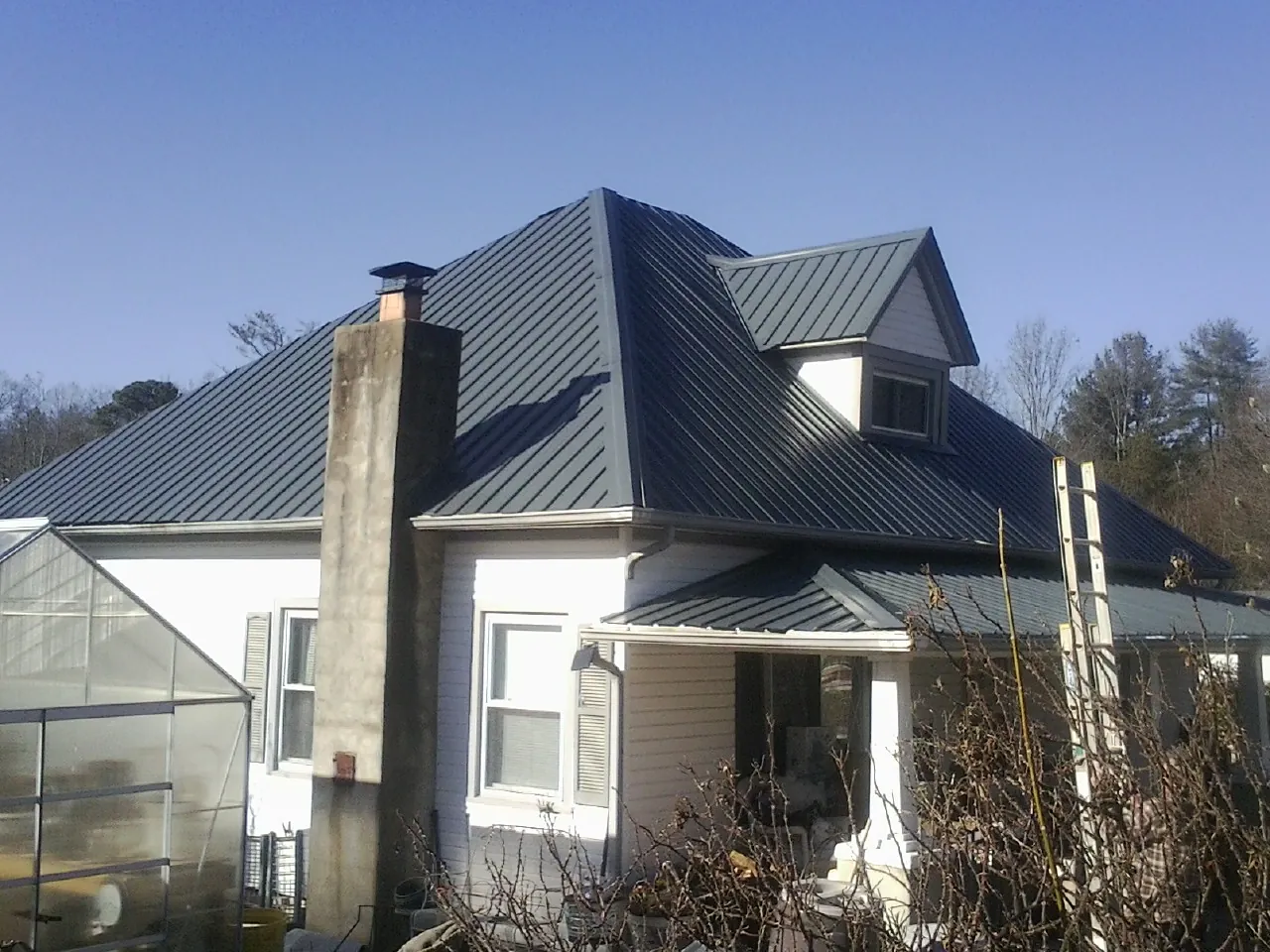 Dark blue standing seam metal roof on a white farmhouse with dormer — Slate & Tile Roof Repair by Roofing Brothers in East Quogue