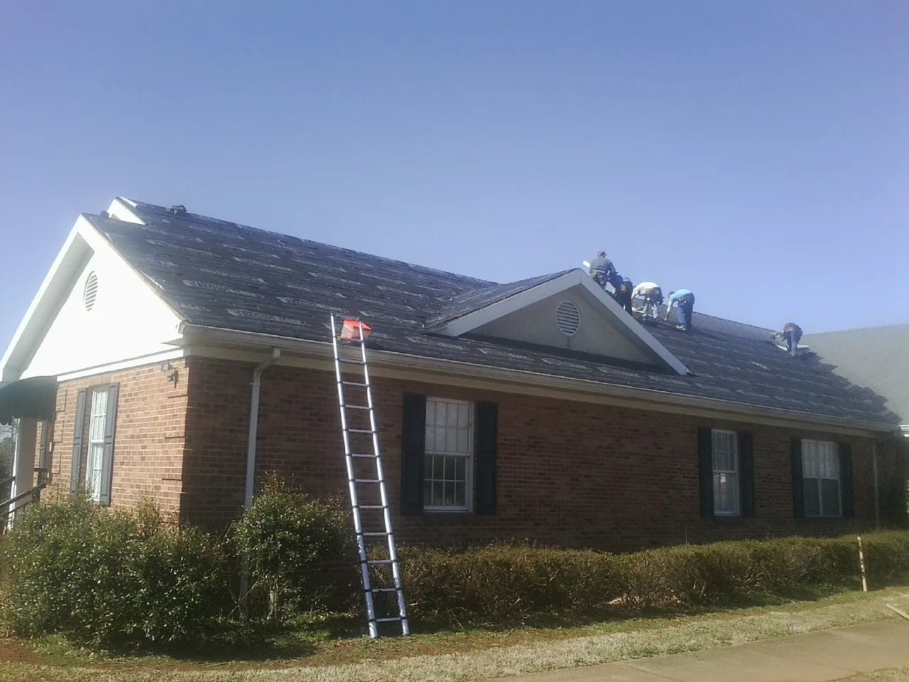 Crew tearing shingles off a brick ranch roof with a ladder set — Metal Roof Repair work by our crew in East Quogue