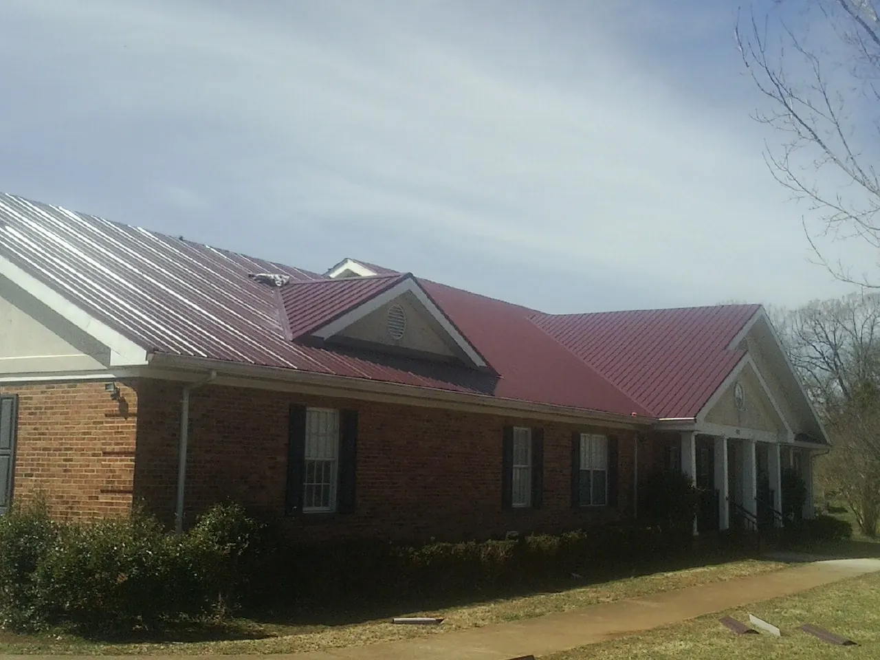 Red metal roof with gabled entries on a long brick building, from a Hail Damage Roof Repair job in East Quogue