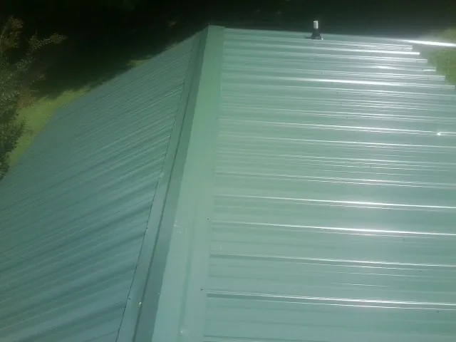 New green metal panels meeting at the ridge of a roof — Flat Roof Repair work by our crew in East Quogue