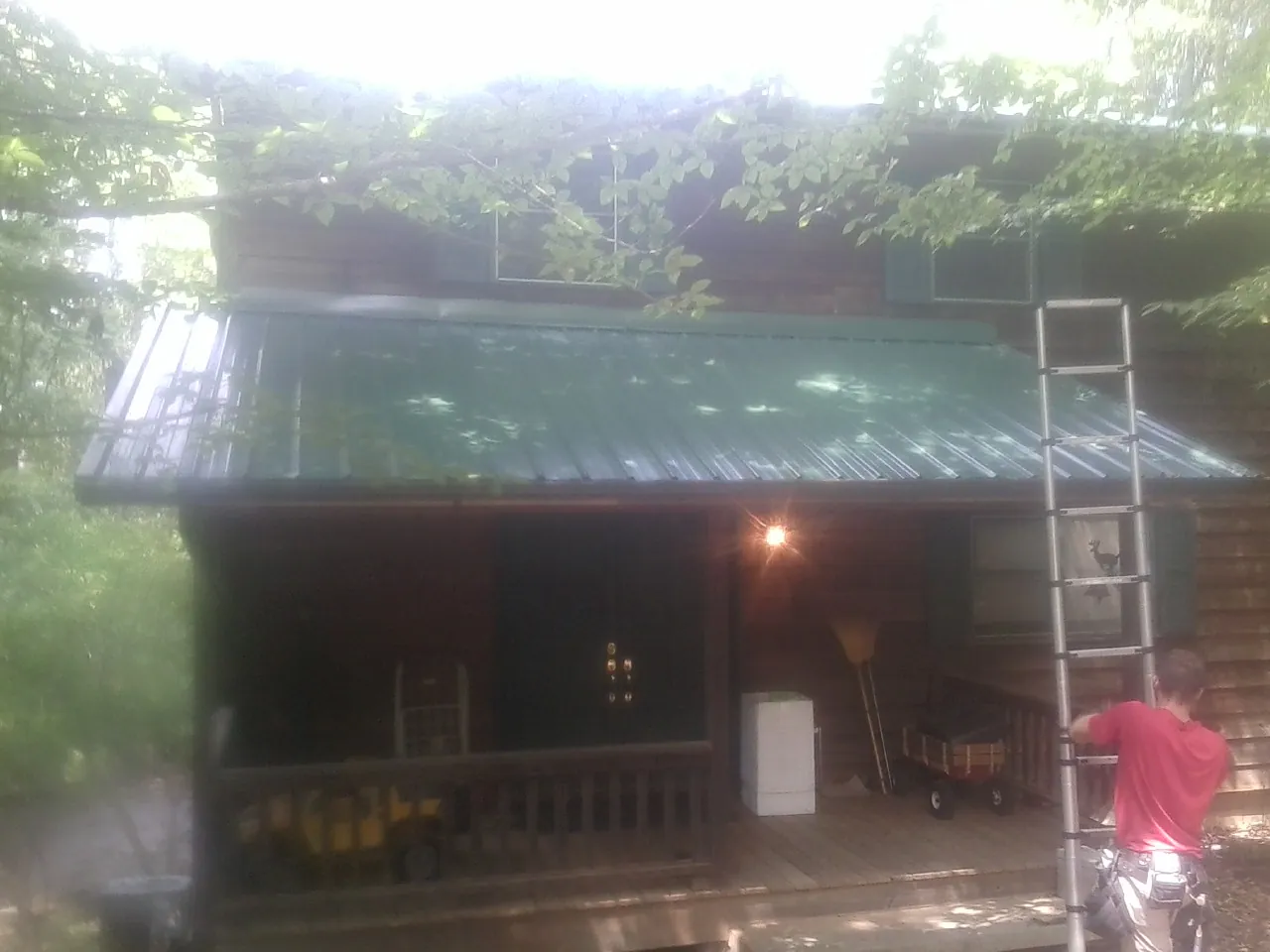 Worker on a ladder at the green porch roof of a wooded cabin in East Quogue