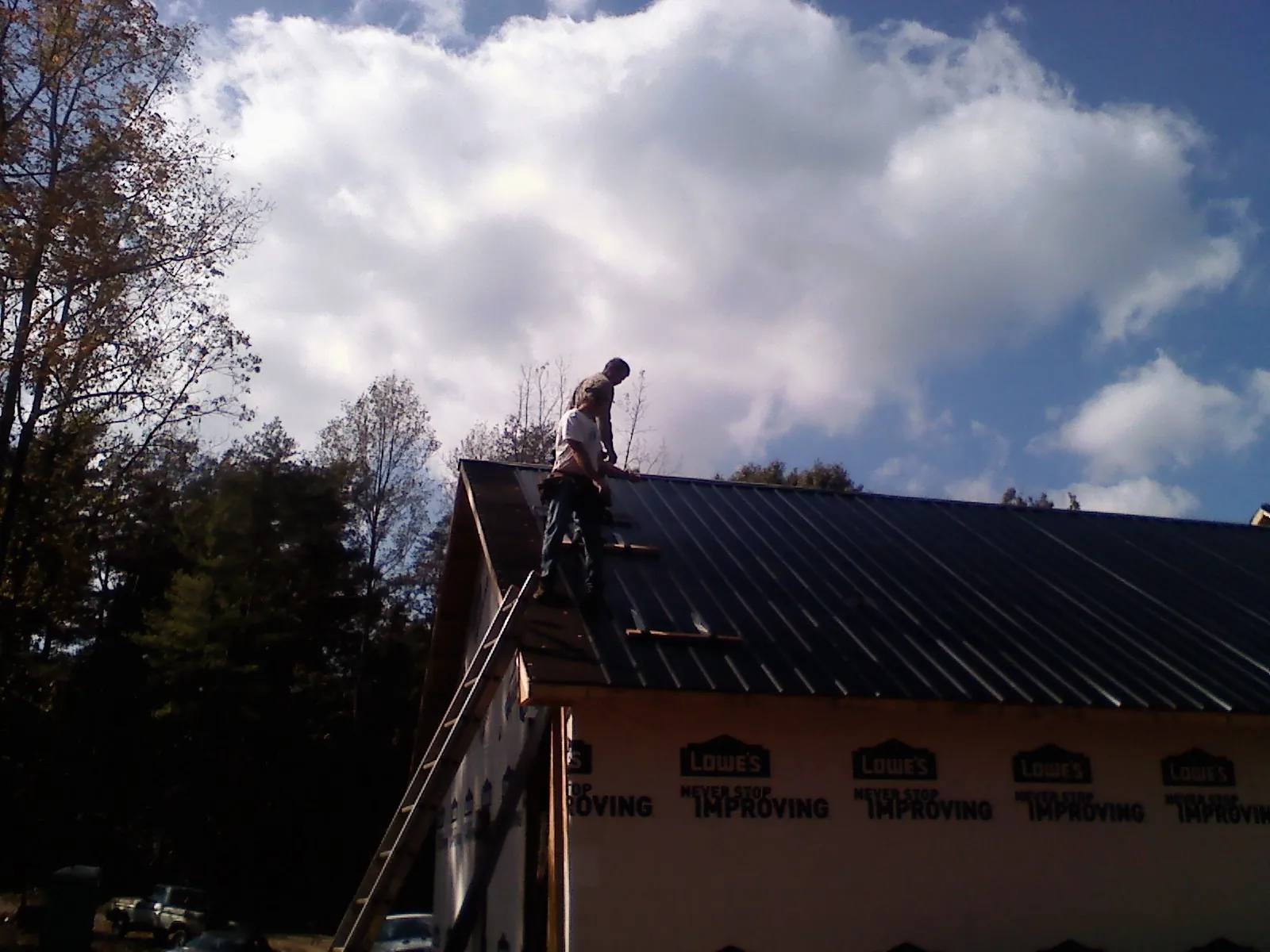 Roofer fastening dark metal panels high against a cloudy sky, from a Roof Inspection job in East Quogue