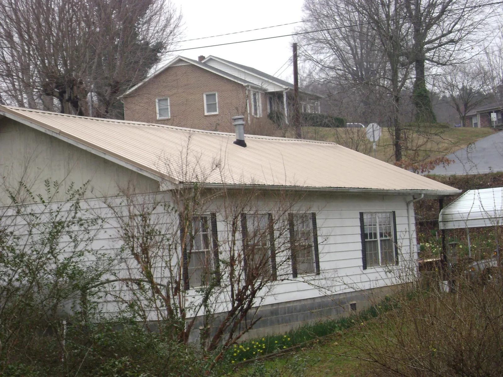 Tan metal roof on a white sided house set into a hillside — Commercial Roofing by Roofing Brothers in East Quogue
